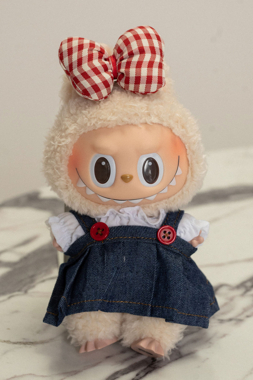 Plush cream-colored Labubu doll wearing a red-and-white checkered bow, denim dress with buttons, and red accents.