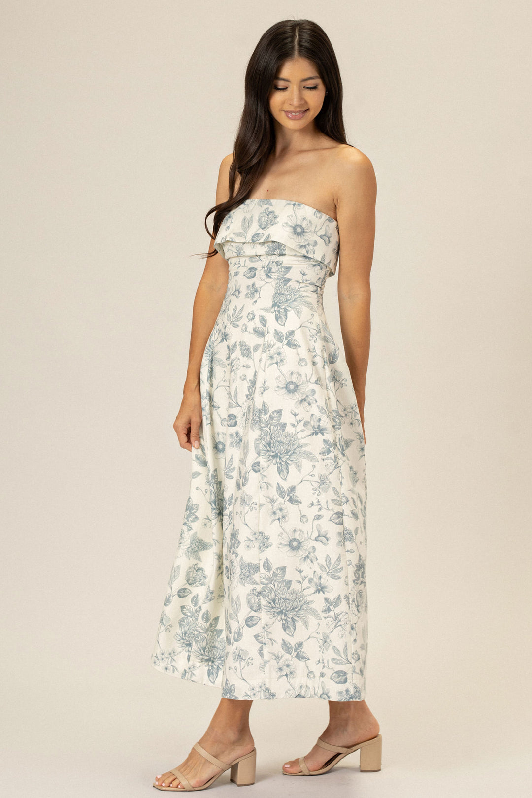 A strapless midi dress with a floral print in shades of blue and gray, featuring a ruffled neckline and a fitted silhouette.