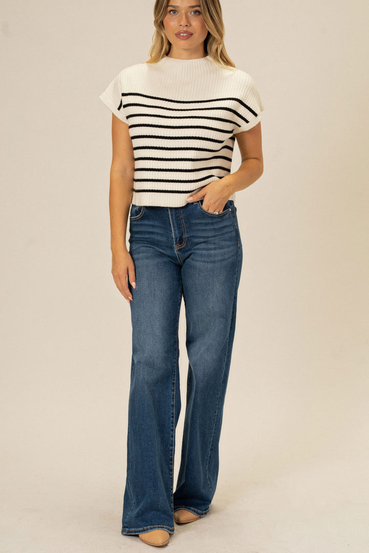 A fitted, cream-colored knit top with horizontal black stripes, worn with high-rise, dark-wash denim jeans by a young, blonde woman.