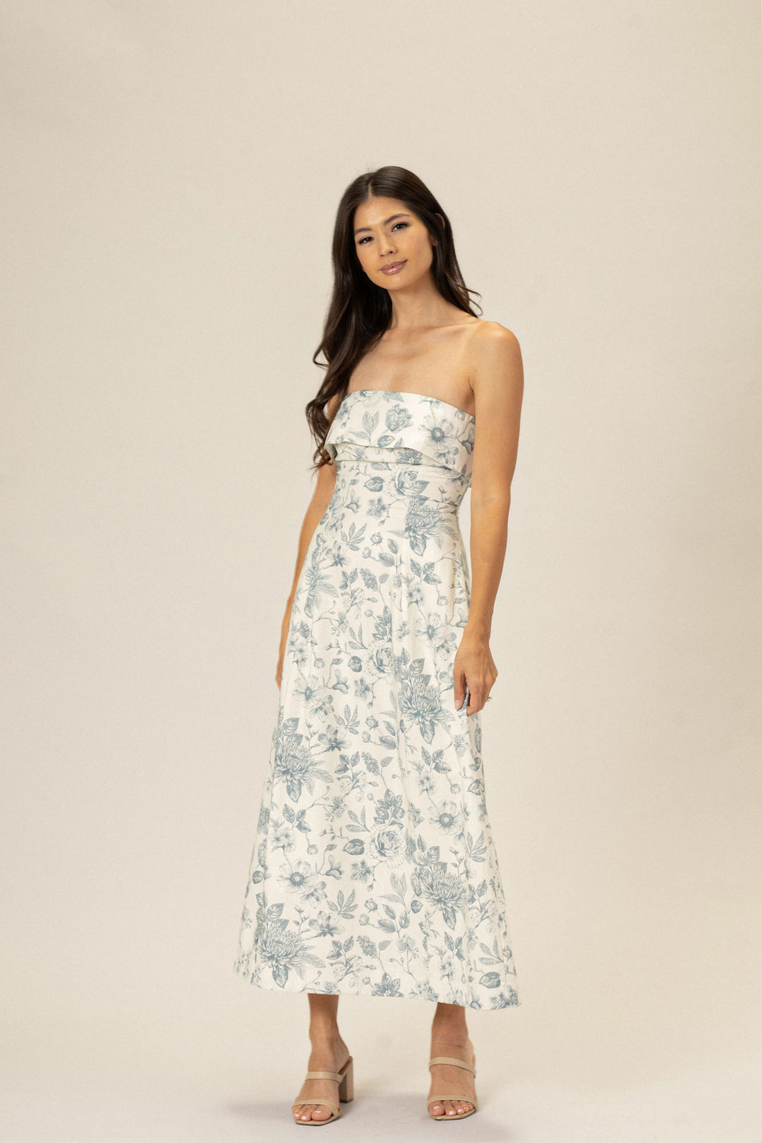 A strapless midi dress with a white background and a delicate floral print in shades of blue, featuring a ruffled bodice and a flowing skirt.