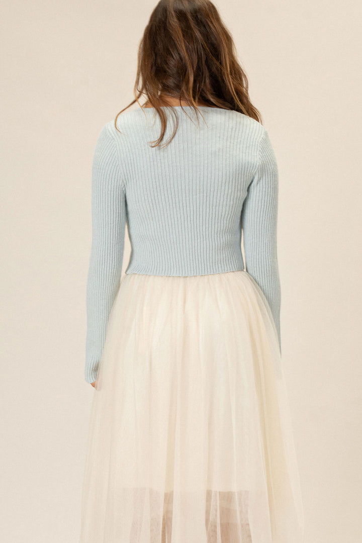 A cropped long-sleeve knit top in a pale blue color, with a ribbed texture, paired with a flowy cream-colored tulle skirt.