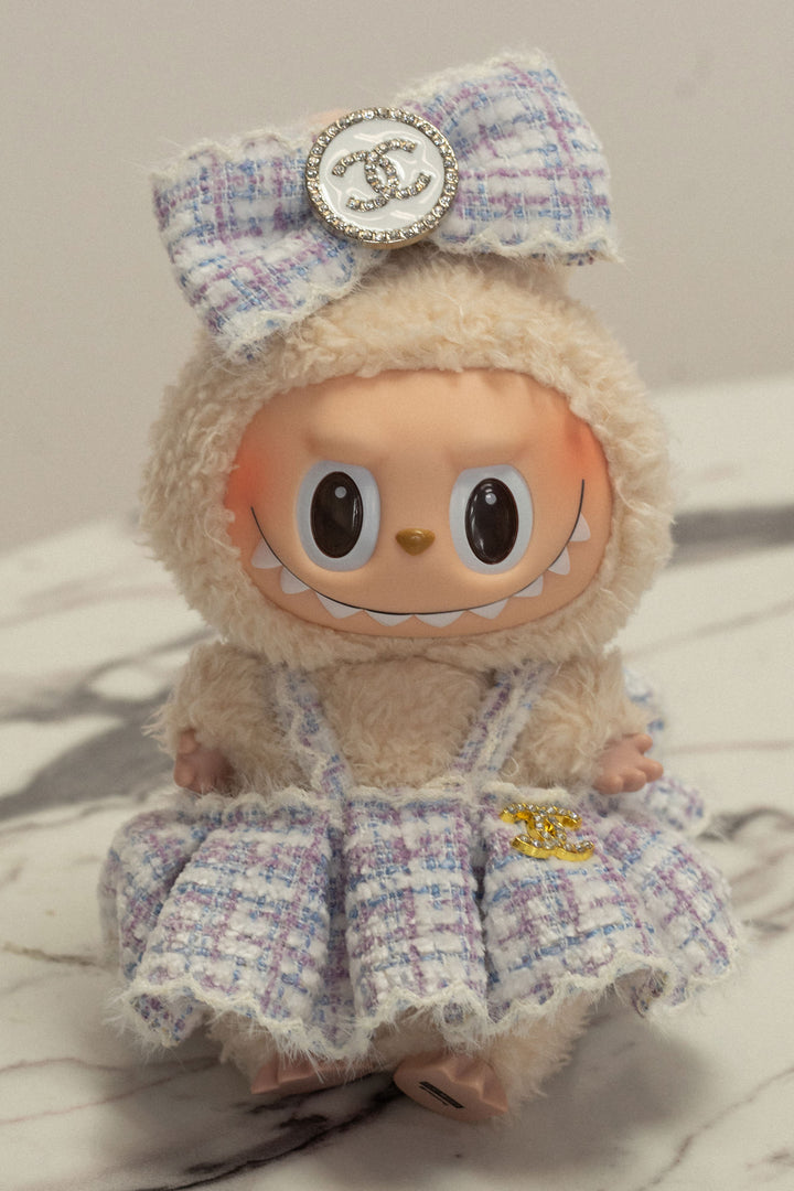 Plush lavender and white tweed doll with oversized eyes, metallic bow, and Chanel-inspired branding.