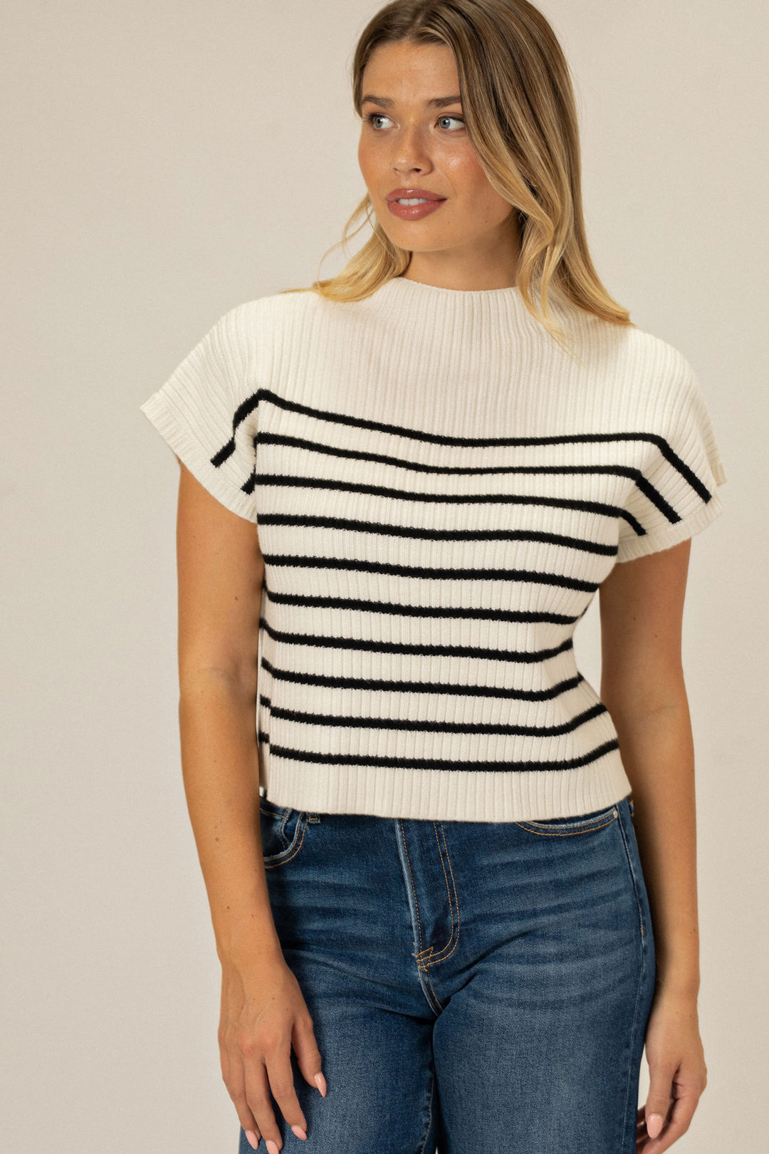 A ribbed knit top in an off-white and black striped pattern, featuring a mock neck and short sleeves.