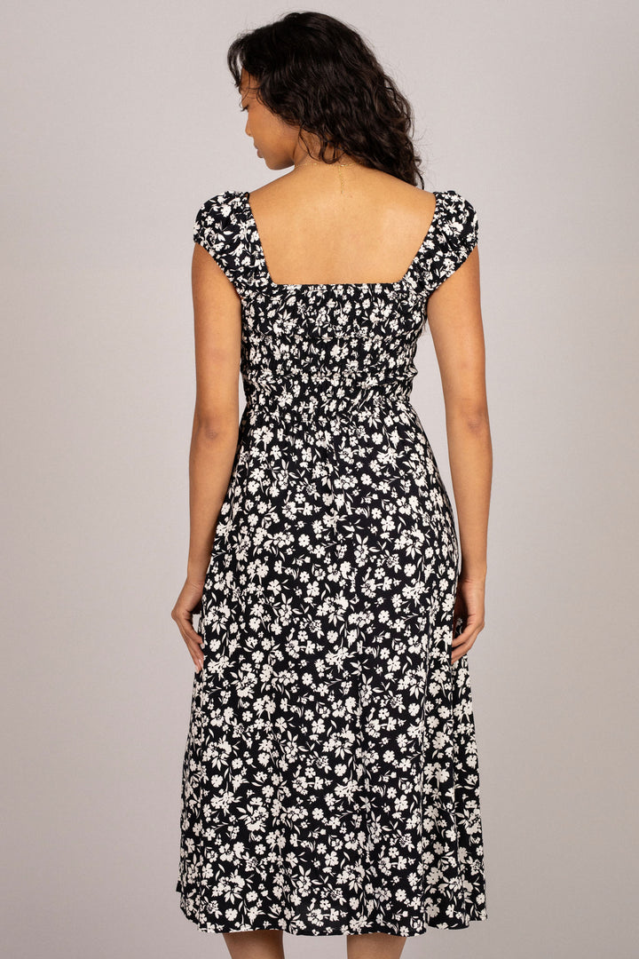 A black midi dress with a floral print pattern, smocked bodice, and puffed sleeves, showcasing a feminine and whimsical design.