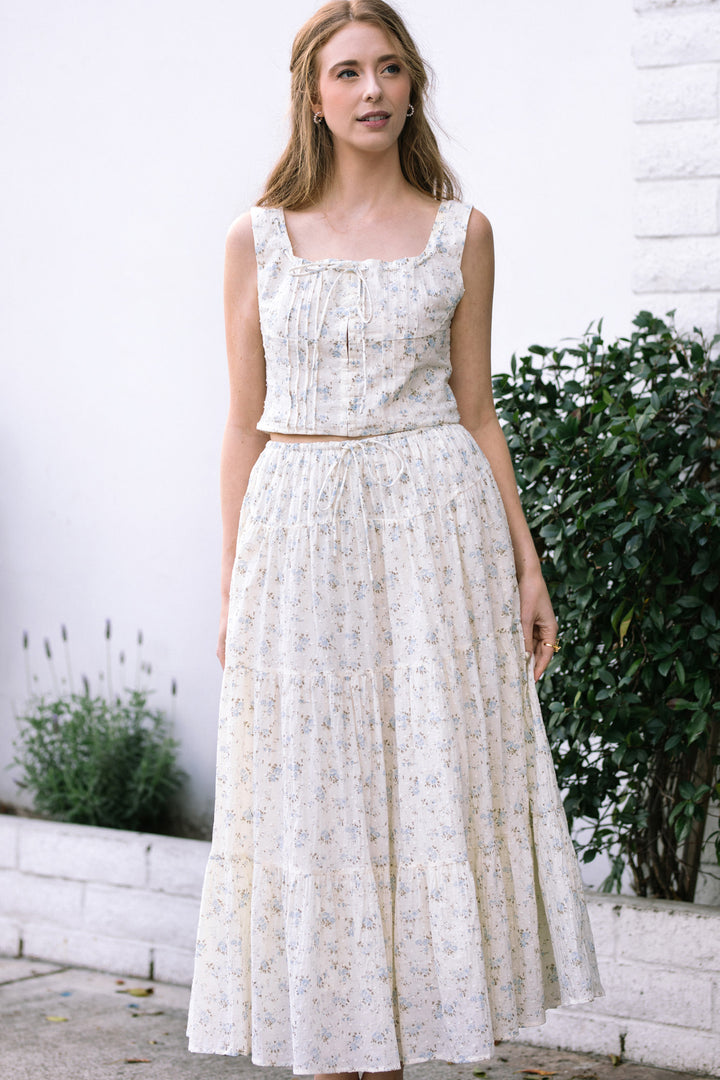 A white sleeveless blouse with a puffed bodice and a flowy, knee-length floral print skirt, perfect for a spring or summer look.