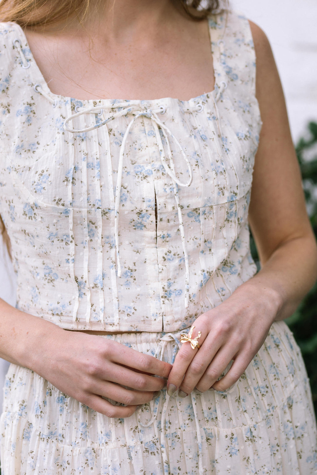 A white floral-patterned sleeveless dress with a tie detail at the bust and waist, creating a feminine and charming look.