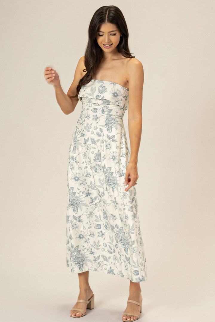 A floral print dress with a strapless, ruffle-trimmed neckline, fitted waist, and a flowing, ankle-length skirt in a soft, muted color palette.