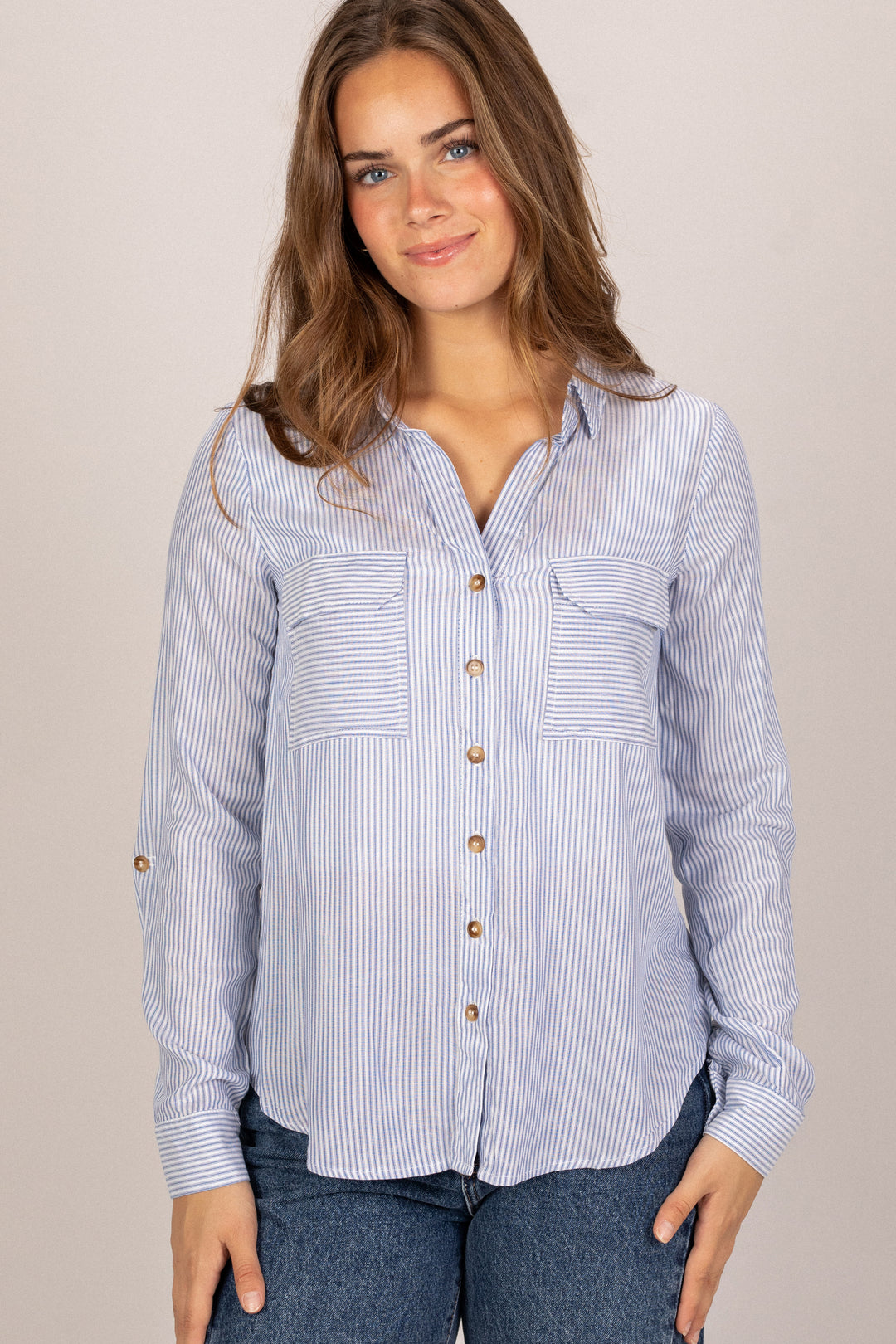 A striped button-up blouse with a relaxed fit, wooden buttons, and two chest pockets, modeled by a woman with wavy brown hair.