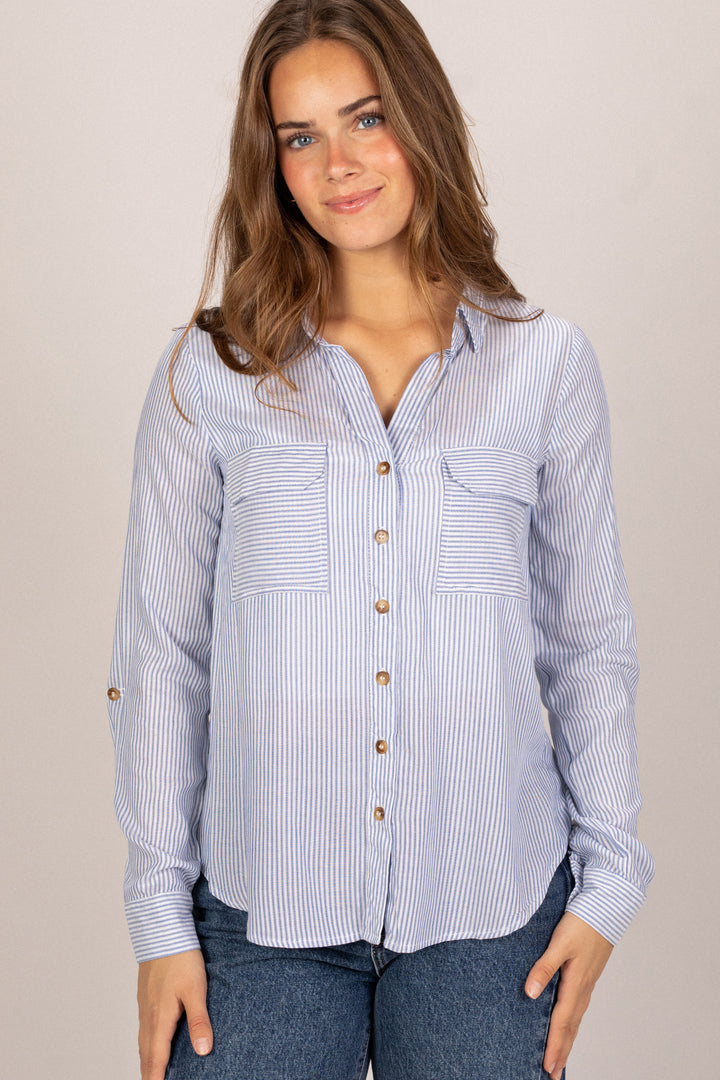 A striped button-up blouse with a relaxed fit, wooden buttons, and two chest pockets, modeled by a woman with wavy brown hair.