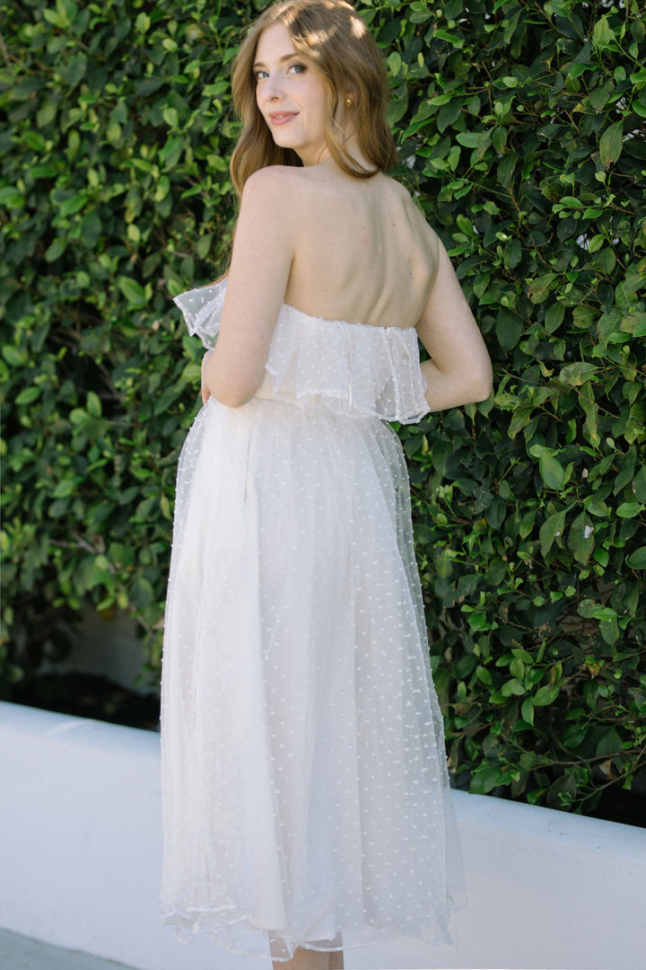 A beautiful off-the-shoulder midi dress made of delicate white tulle with a ruffled bodice and flowing skirt, perfect for special occasions.