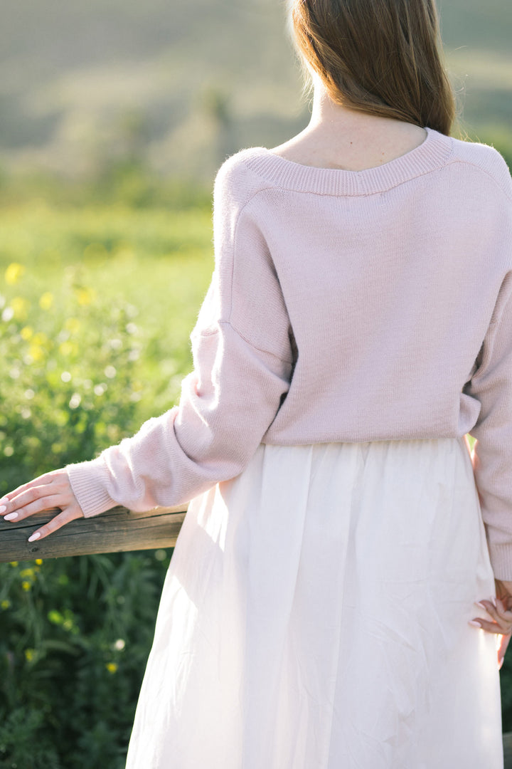 A cozy, light pink cardigan with delicate heart-shaped buttons, featuring long sleeves and a relaxed, comfortable fit.