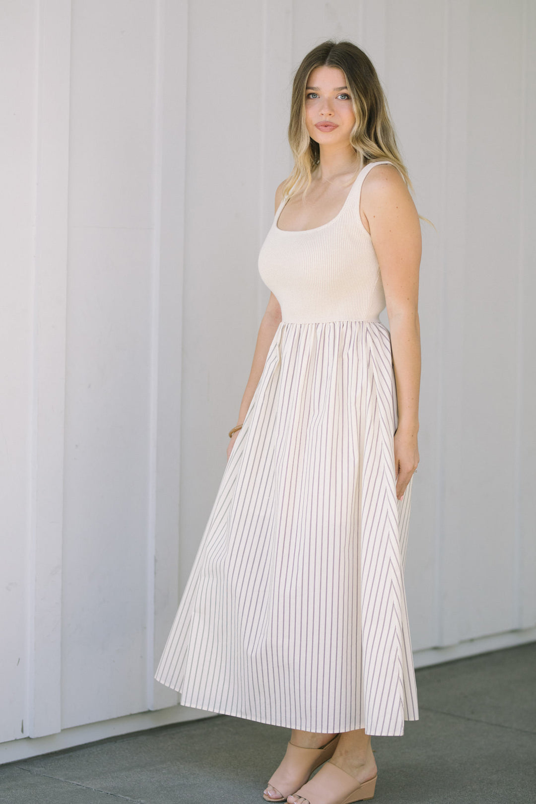 A woman wearing a sleeveless white dress with a striped skirt, featuring a scoop neckline and a fitted bodice.