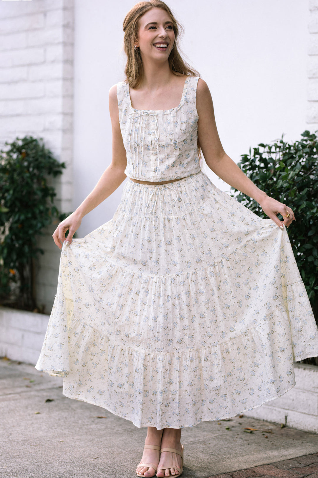 A white, floral-patterned sundress with a pleated bodice, full skirt, and adjustable waistband that flows gracefully.