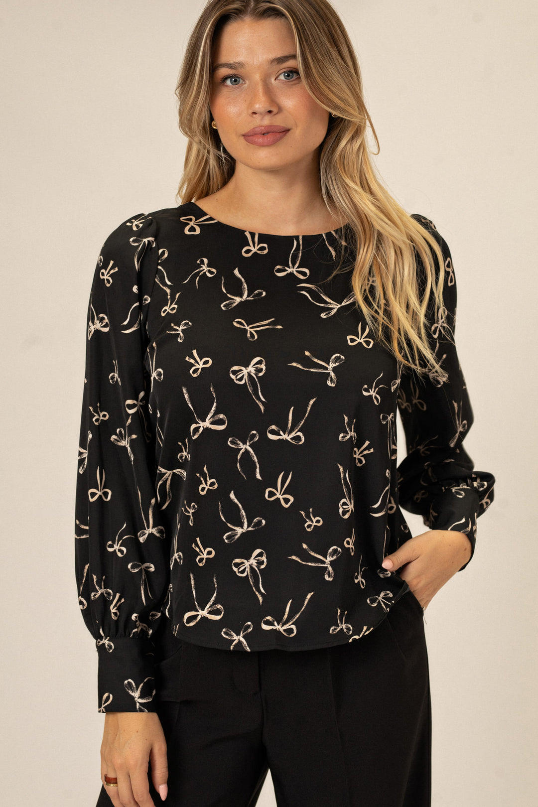 A black long-sleeve blouse with an allover bow print, featuring puffed shoulders and a flattering silhouette.