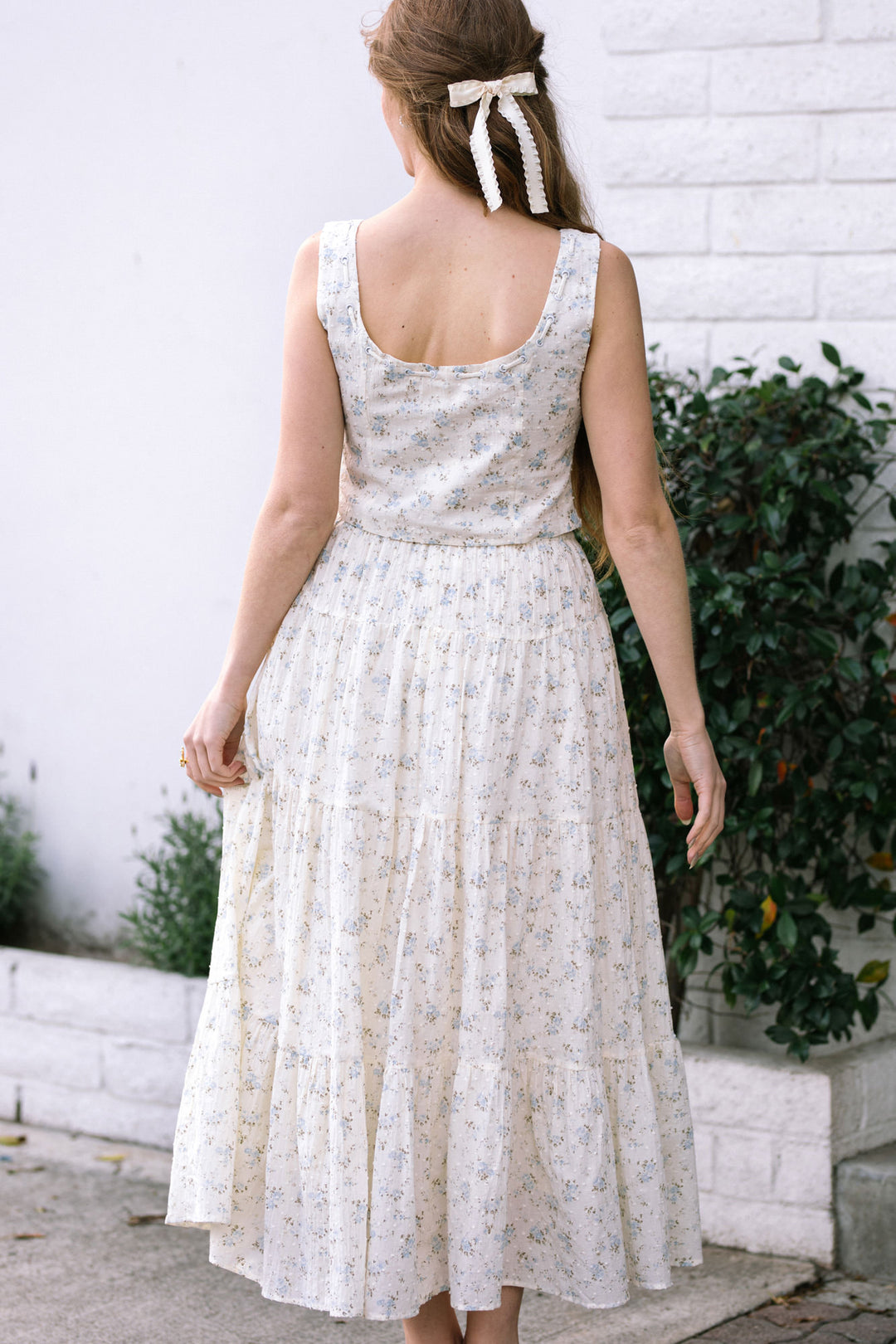 White floral print sleeveless dress with a pleated midi-length skirt, finished with a white ribbon bow at the back.