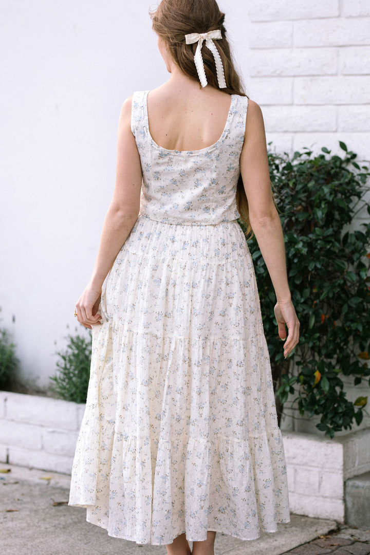 White floral print sleeveless dress with a pleated midi-length skirt, finished with a white ribbon bow at the back.