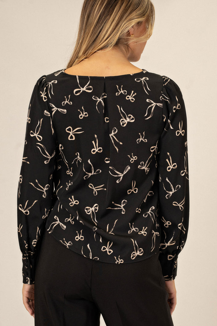 Black long-sleeve blouse with allover white bow print, puffed shoulders, and button closure at back.