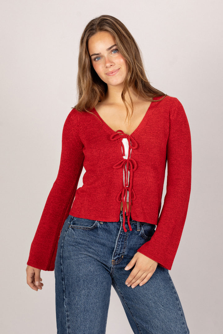 A young woman in a form-fitting red sweater with a tie-front detail, paired with high-waisted blue jeans.