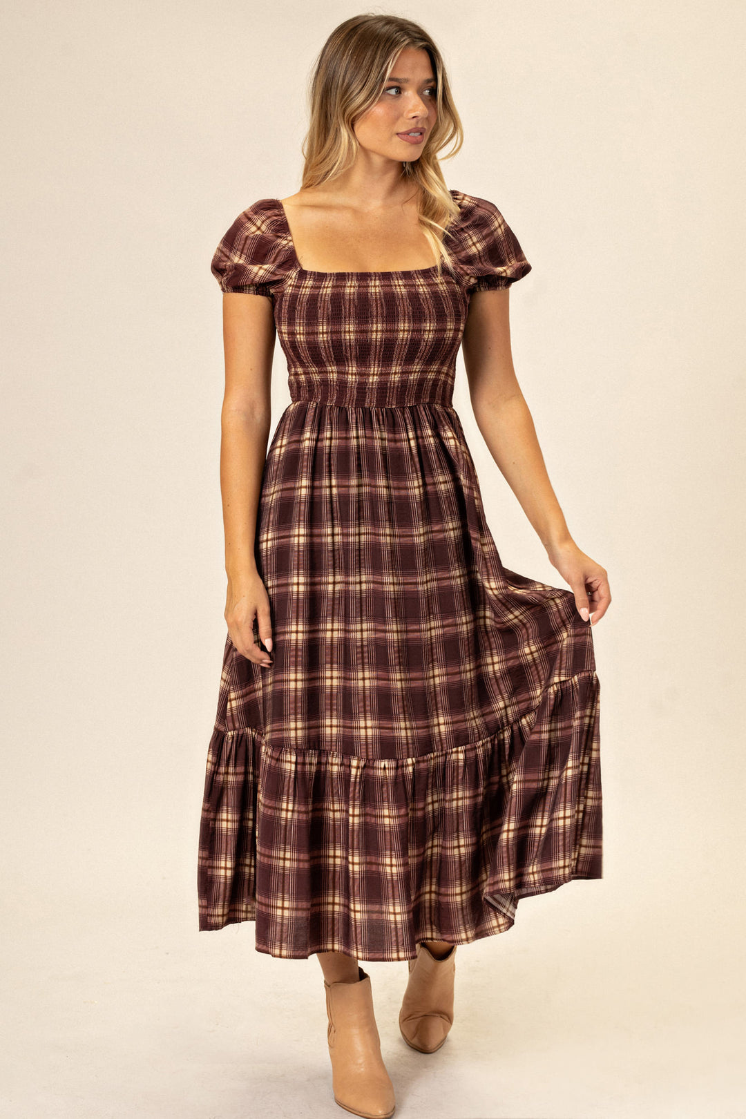 A burgundy and tan plaid maxi dress with a fitted bodice, puff sleeves, and a flowy, tiered skirt.