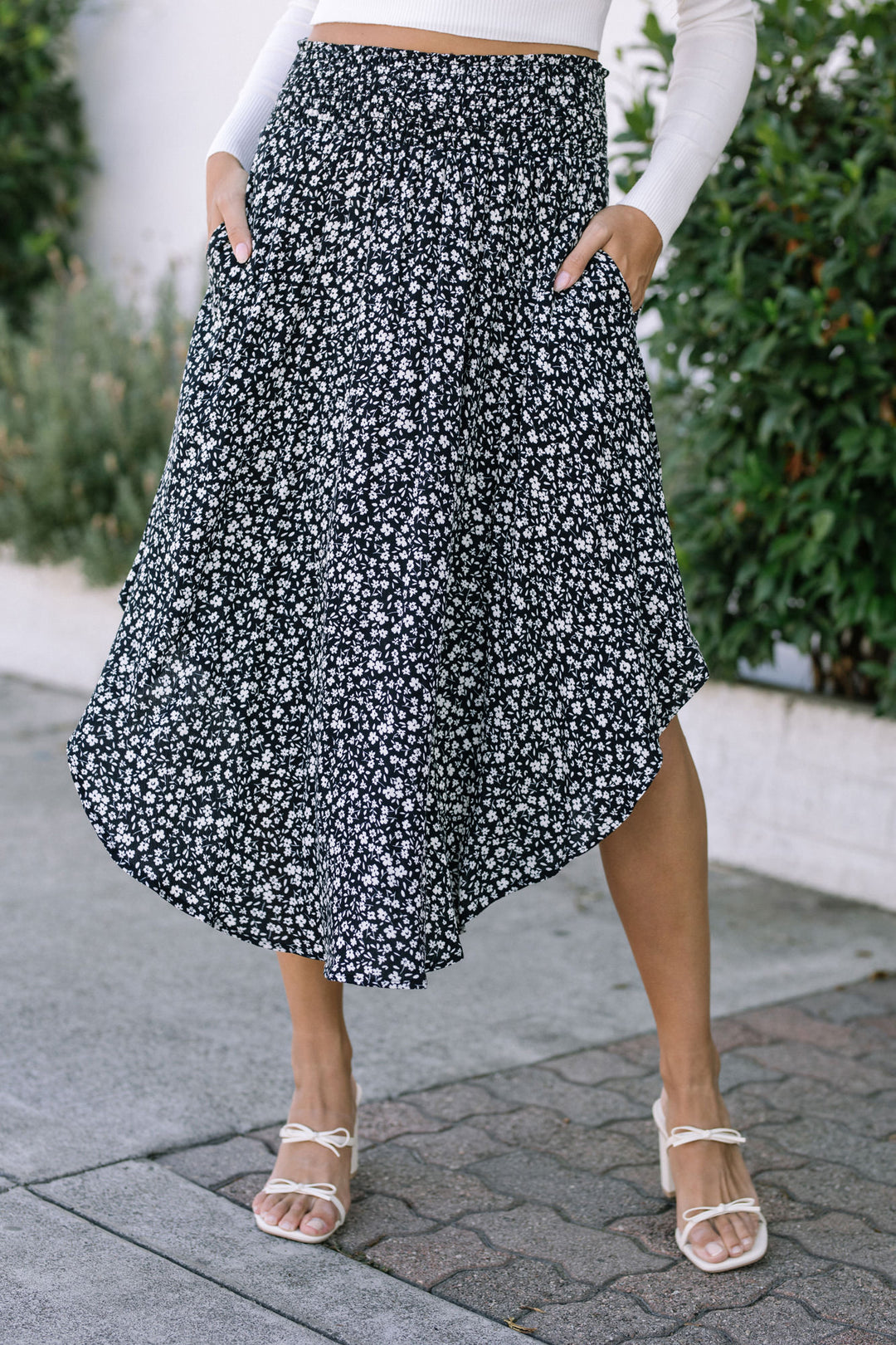 A black and white floral patterned midi skirt with a round hem and pockets, worn with strappy white sandals.