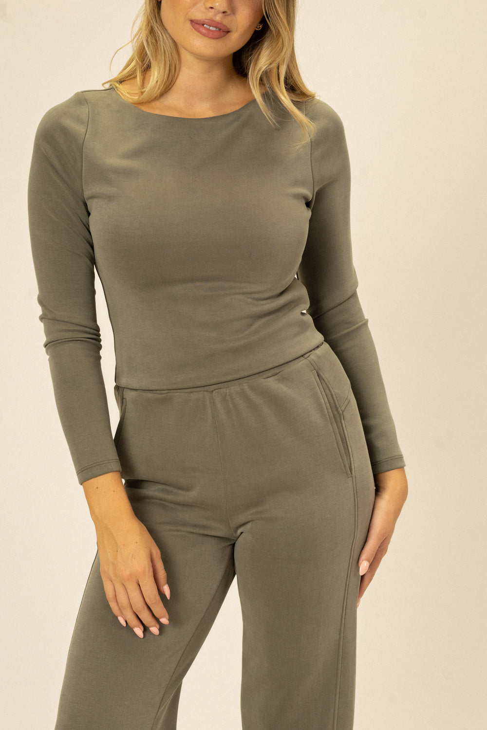 A sage green long-sleeve jersey top with a form-fitting silhouette and a round neckline, modeled by a woman with blonde, wavy hair.