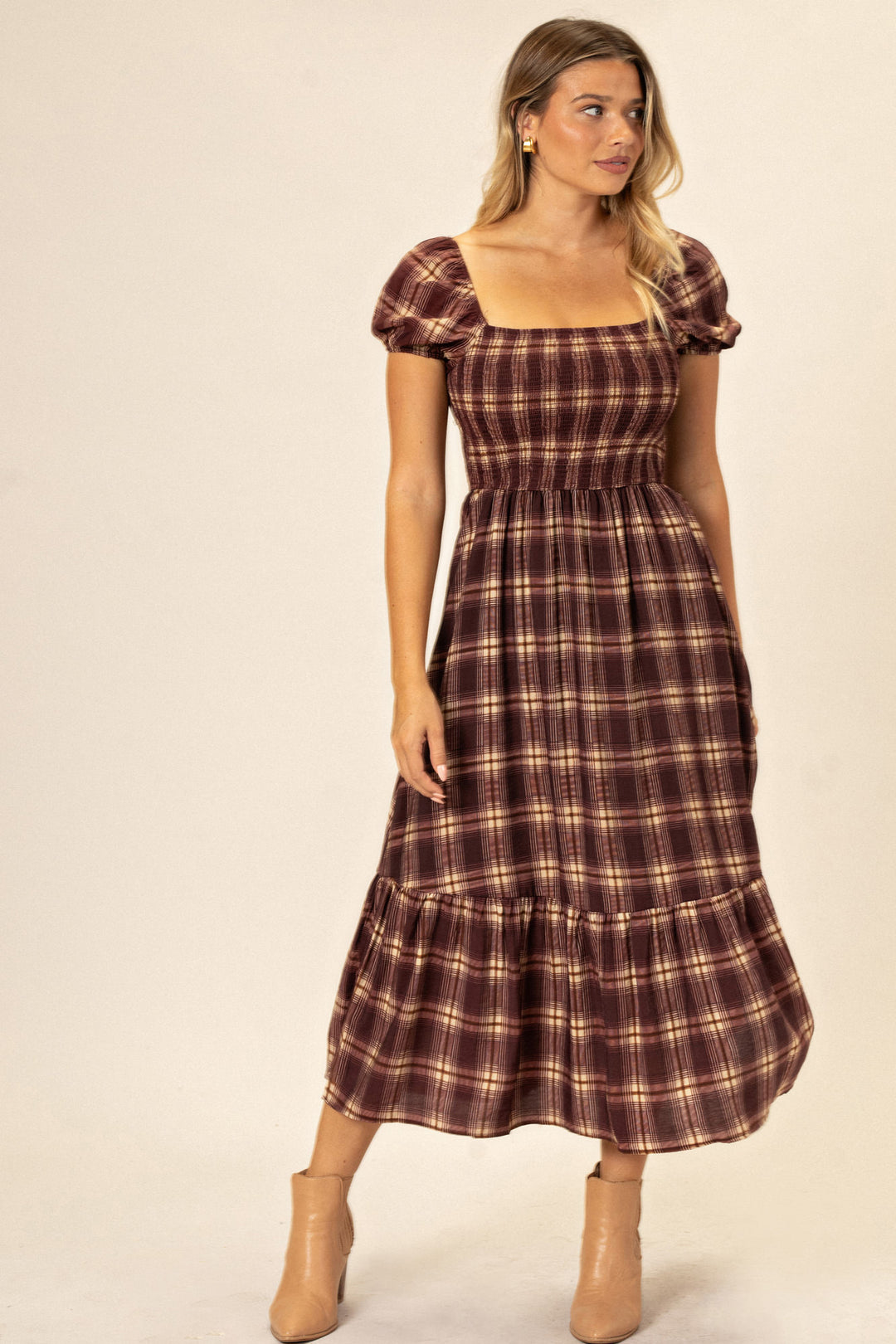 A plaid midi dress with a smocked bodice, short puff sleeves, and a full, tiered skirt in a rustic burgundy and tan plaid pattern.