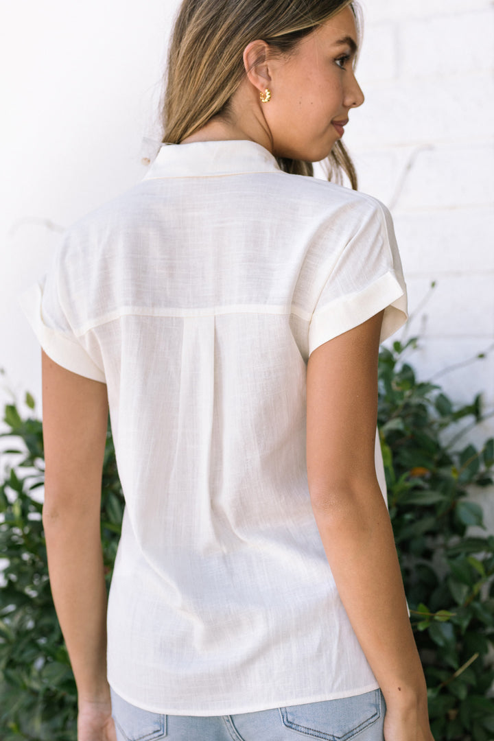 White button-down shirt with pleated back detail, modeled by a woman with long blonde hair against a natural backdrop.