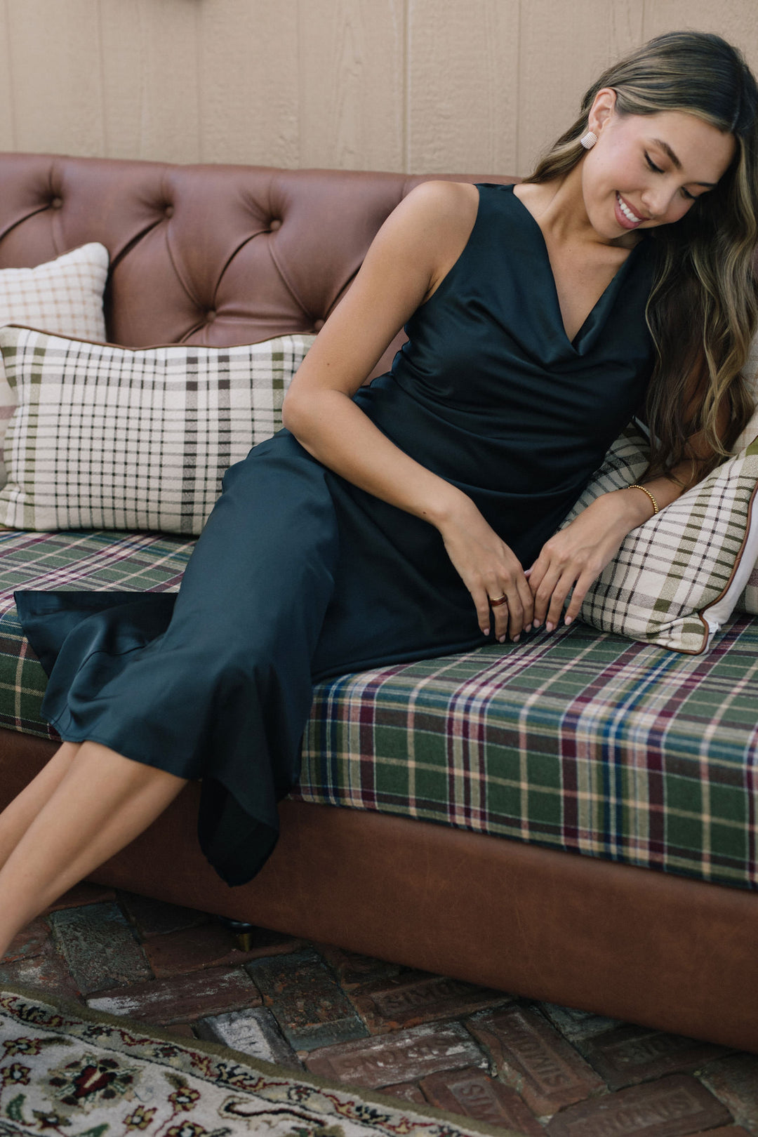 Sleek, dark green satin dress with a cowl neckline, worn by a young woman with long, dark hair sitting on a patterned couch.