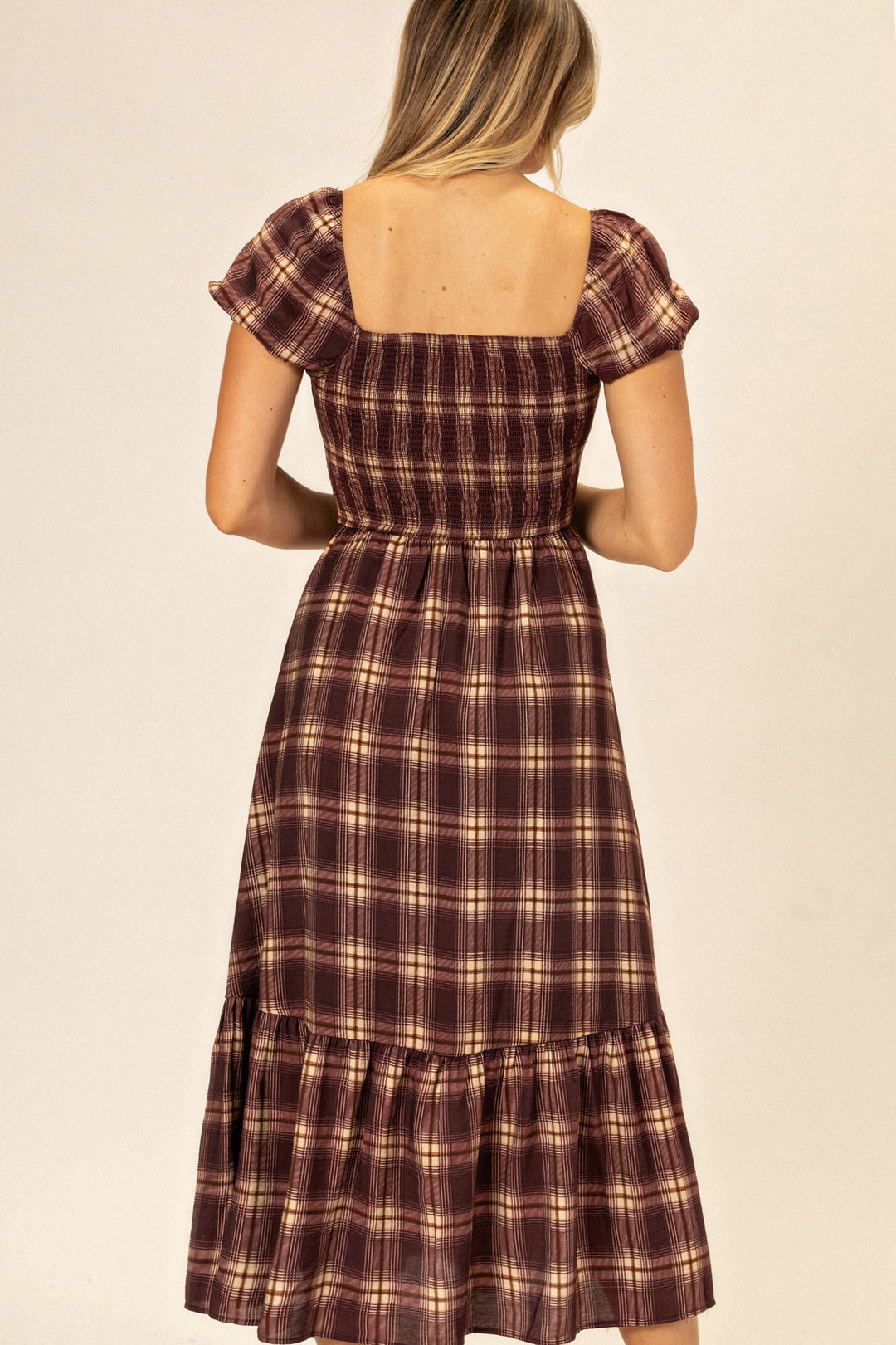 A plaid midi dress with puffed sleeves, a smocked waist, and a tiered skirt in a burgundy and tan color palette.