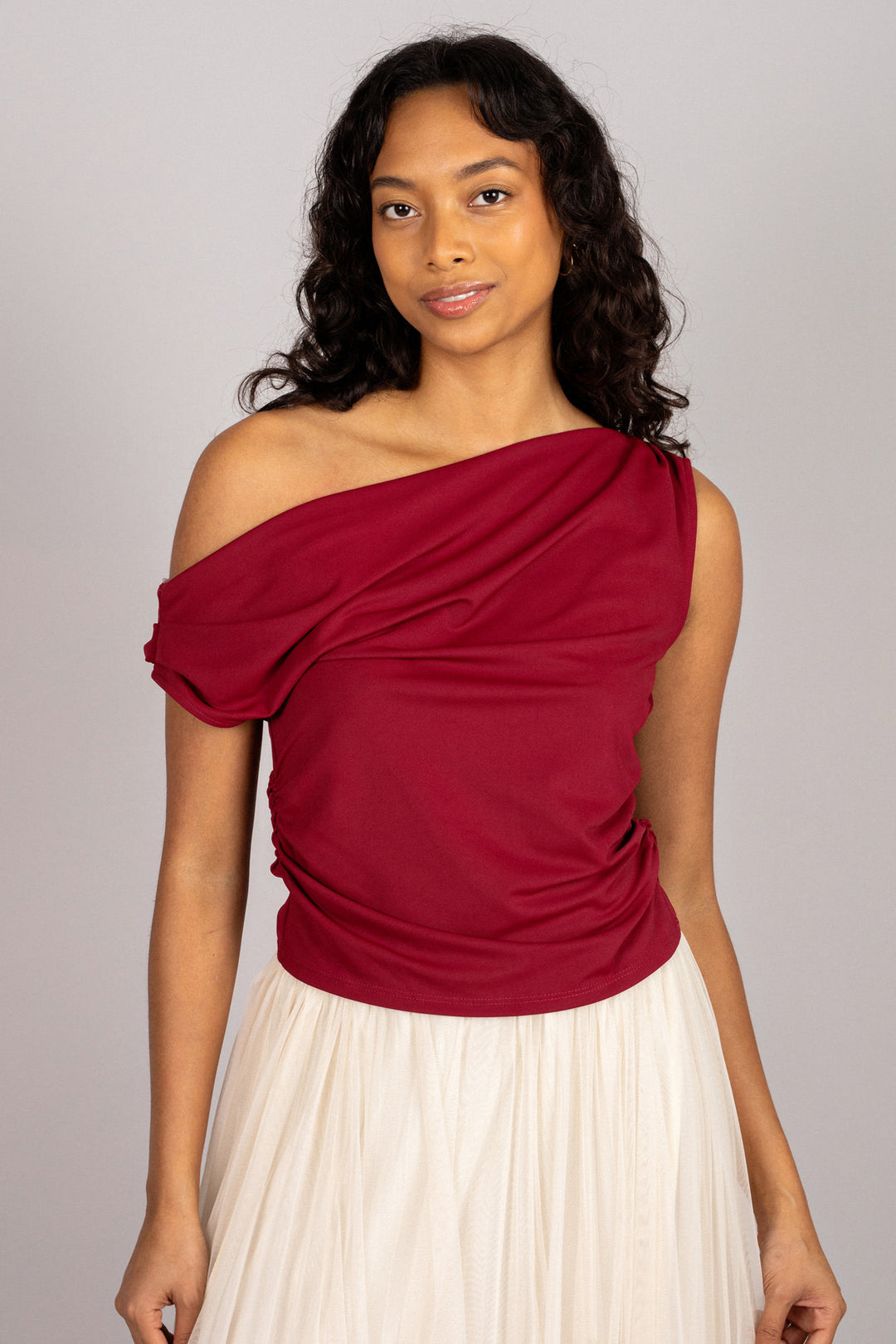 A woman wearing a one-shoulder red top with ruched detailing and a white flared skirt.