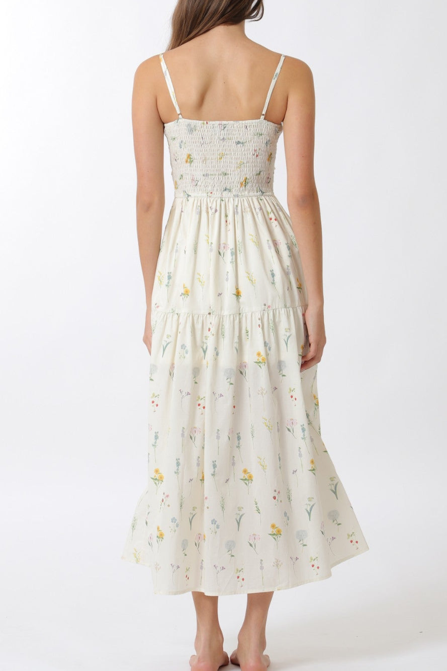A long, flowy maxi dress in a light, off-white shade featuring a delicate, all-over floral print pattern and a smocked bodice.