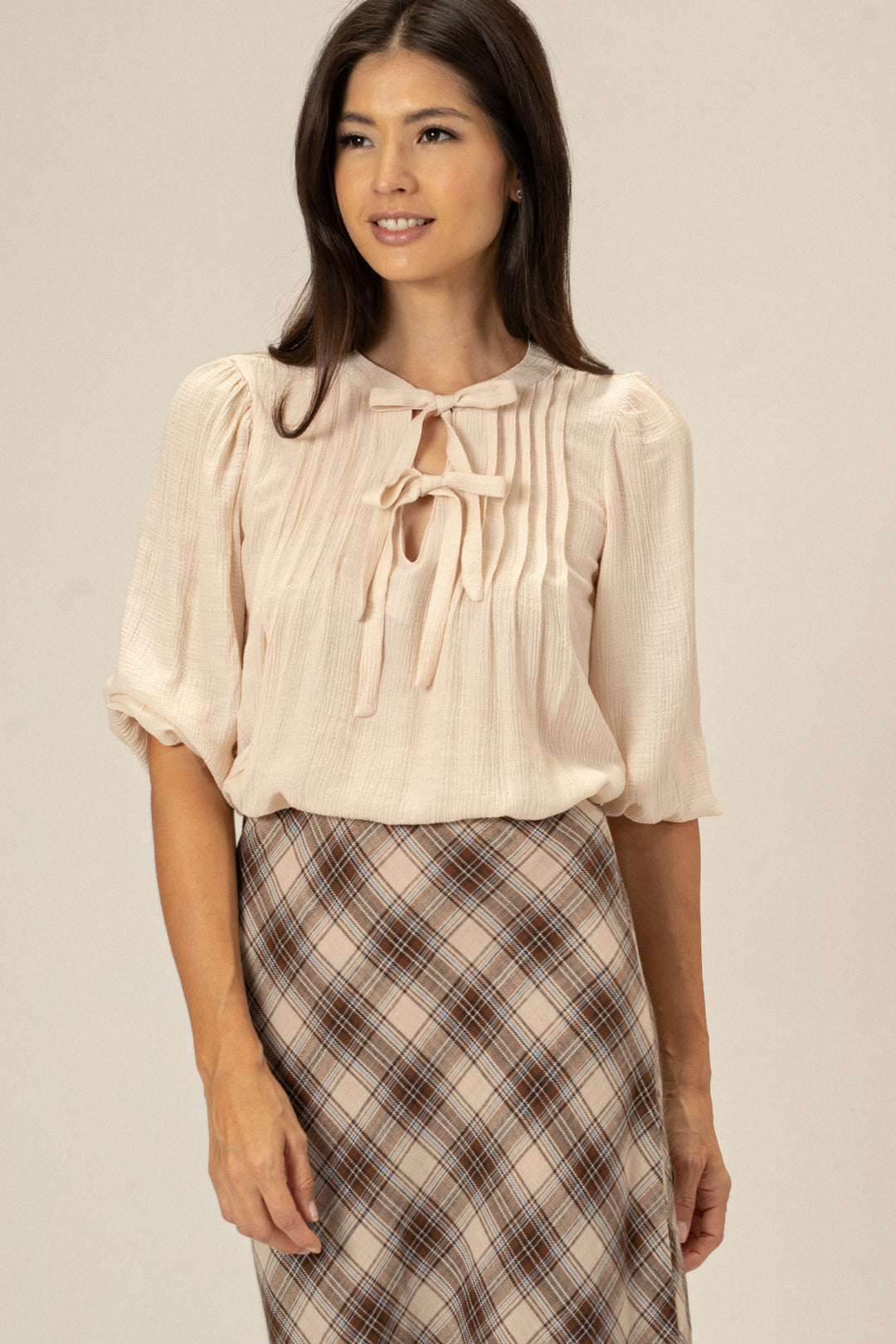 A woman wearing a peach-colored blouse with tie-neck detailing, paired with a plaid skirt.