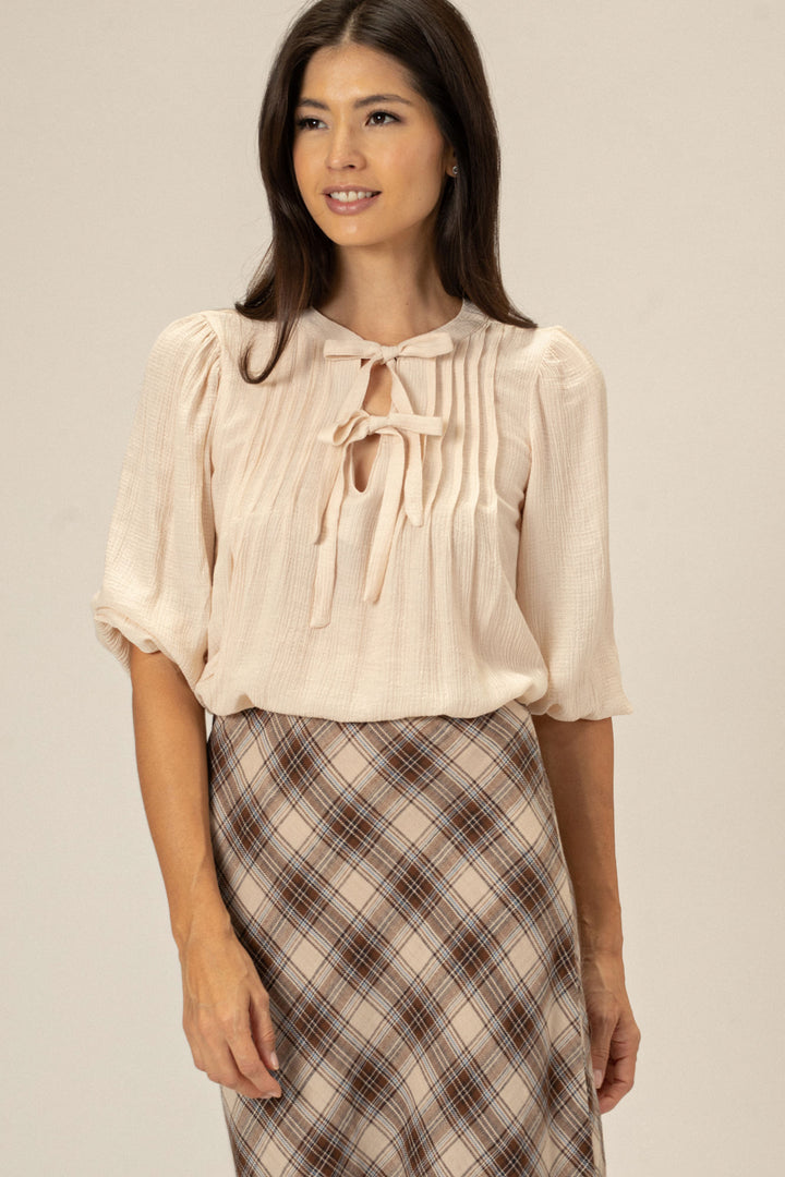 A woman wearing a peach-colored blouse with tie-neck detailing, paired with a plaid skirt.