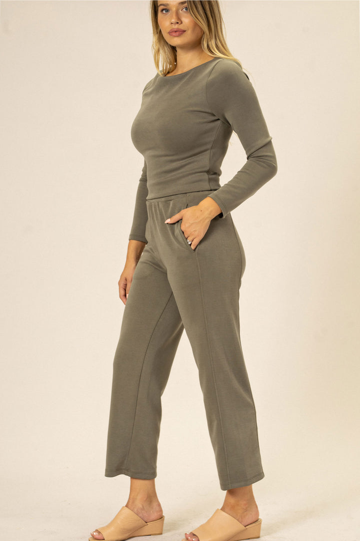 A woman wearing a form-fitting, olive green jumpsuit with long sleeves, a crew neckline, and straight leg pants with pockets.