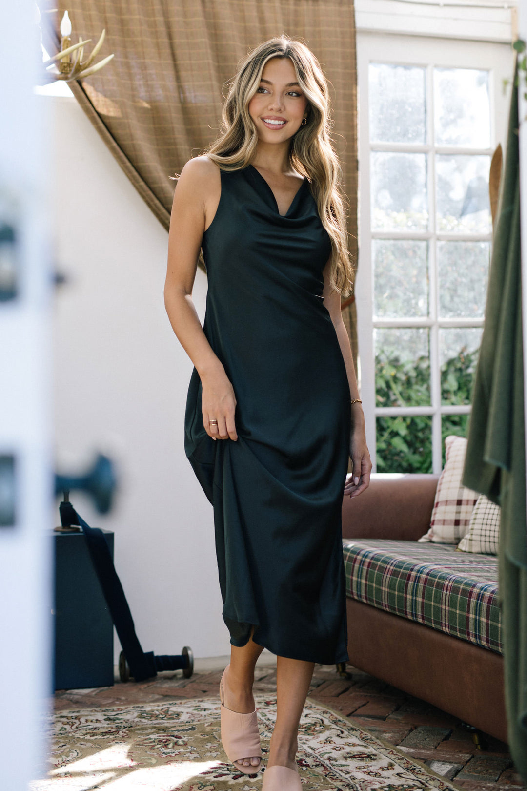 Woman wearing a black cowl-neck satin dress with a flowing, midi-length silhouette.