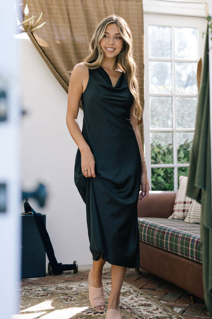 Woman wearing a black cowl-neck satin dress with a flowing, midi-length silhouette.