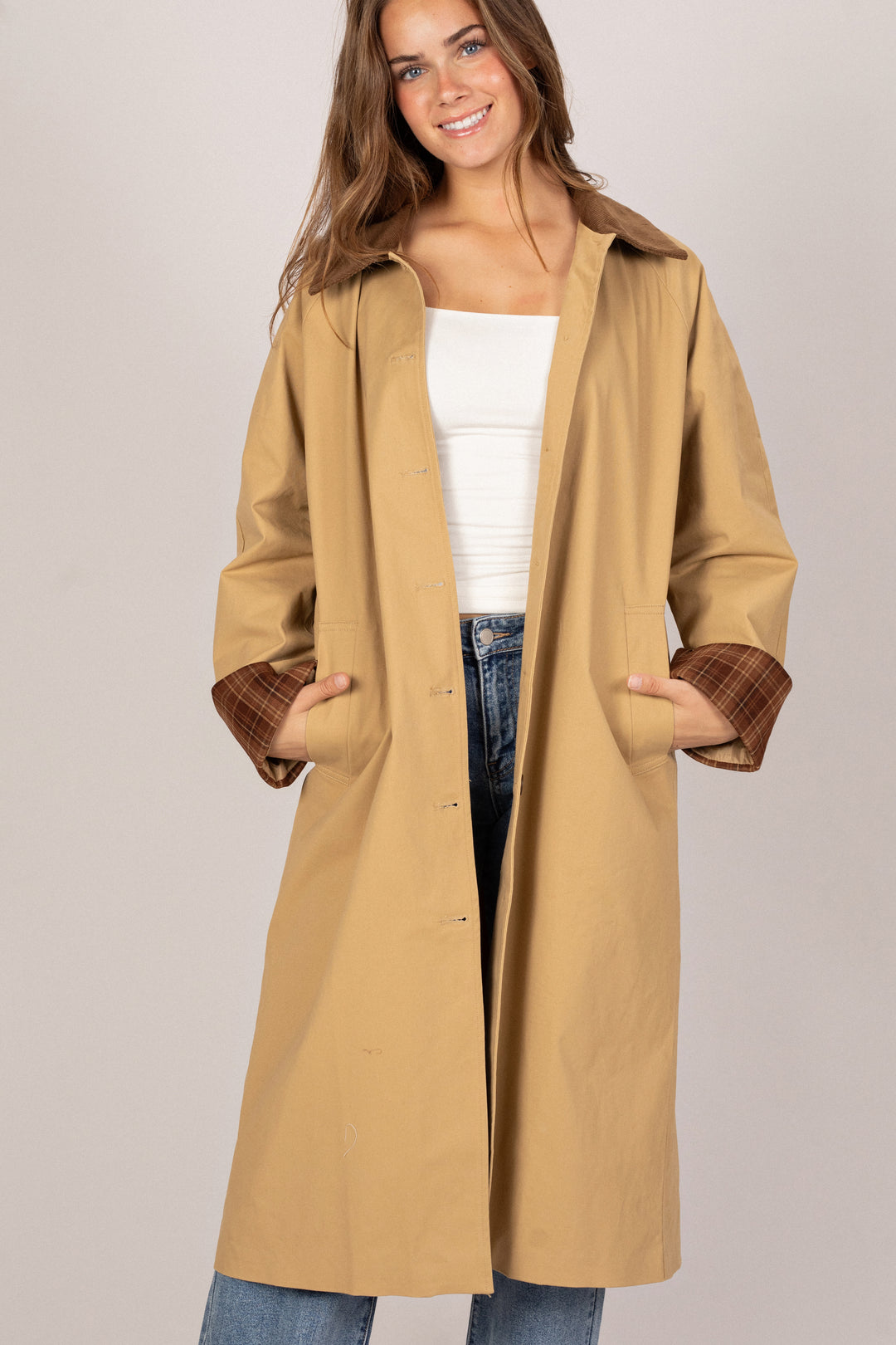 A beige trench coat with a corduroy collar, featuring flared sleeves and a belted waist.