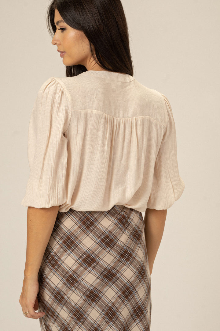 Billowy cream-colored blouse with puffed sleeves and a front tie, paired with a plaid midi skirt.