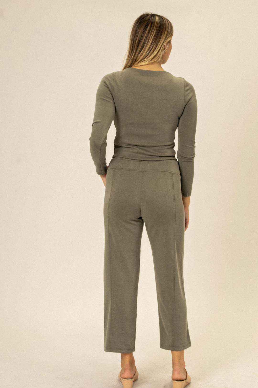 A woman wearing olive-colored straight-leg pants made of soft, stretchy jersey material. The pants have a high-waisted silhouette and a slightly flared leg opening.