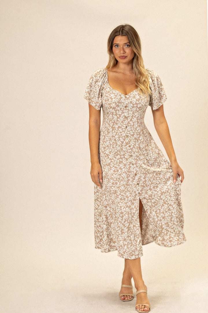 A woman wearing a floral, puff-sleeved midi dress with a v-neckline and side slit, styled with neutral sandals.