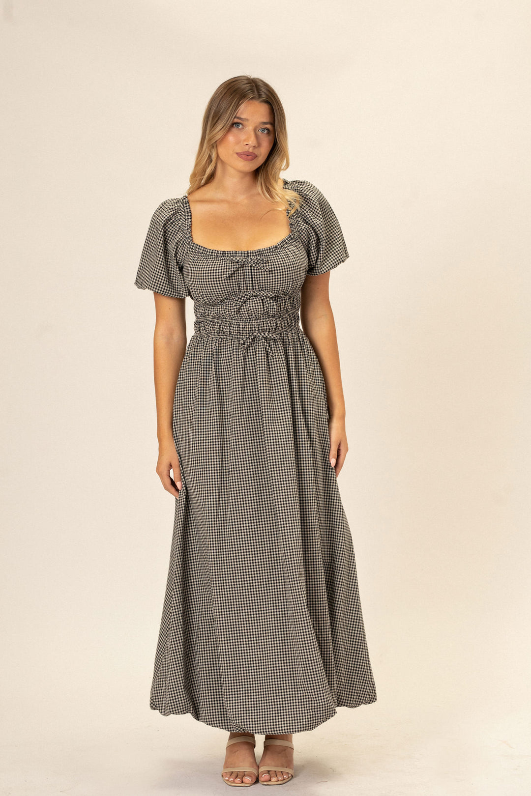 A woman wearing a black and white gingham dress with a bubble hem and puffed sleeves, posing against a white background.