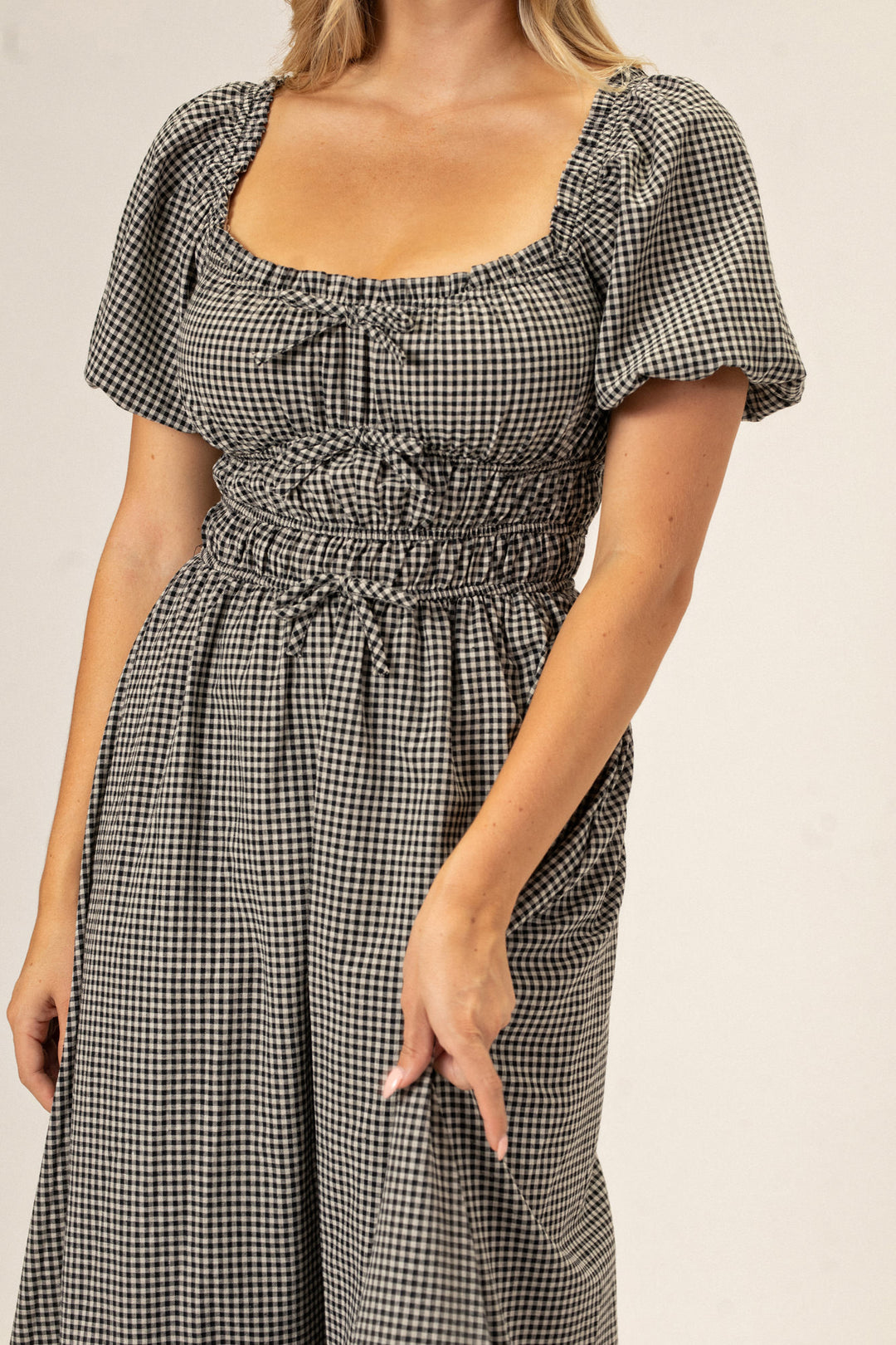 A black and white gingham-patterned dress with a ruffled neckline, puffed sleeves, and a high-waisted, bubble-hemmed skirt.