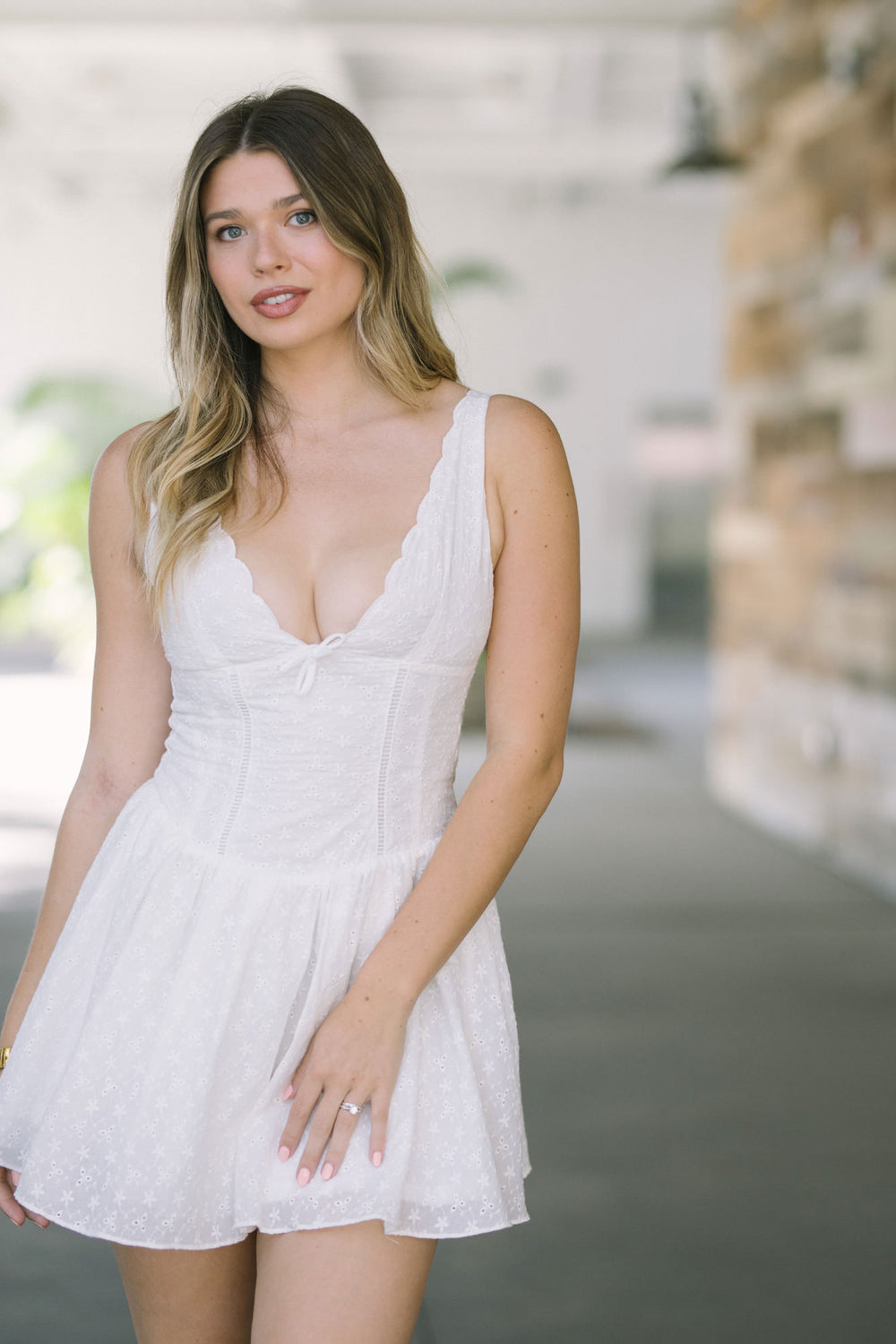White floral eyelet mini dress with scalloped neckline and fitted bodice, captured in full body view against blurred background.