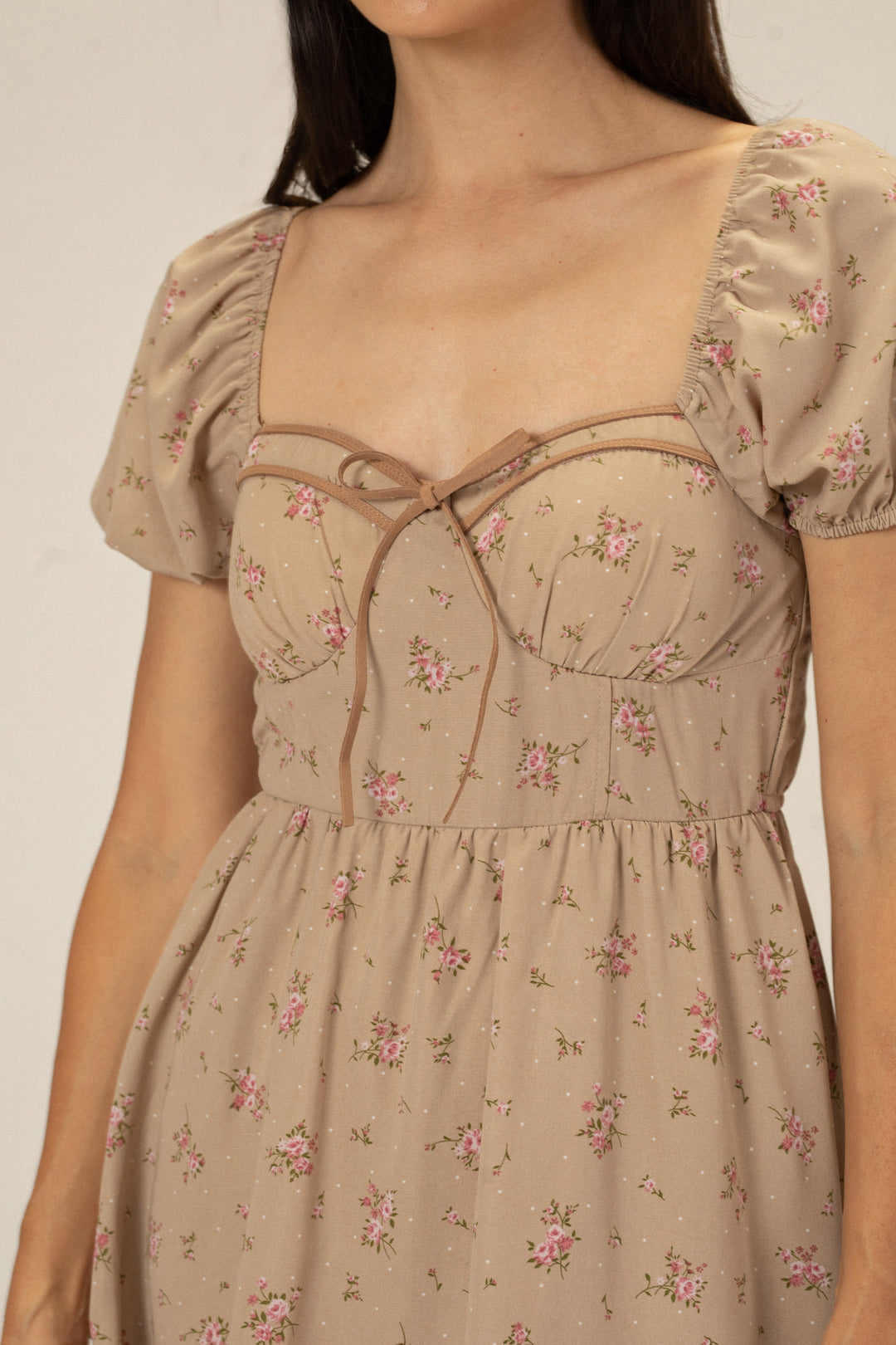A feminine, floral-patterned dress in a light beige tone, featuring puffed sleeves, a cinched waist, and a flowy, above-the-knee skirt.