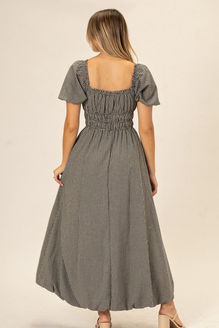 Gingham-patterned dress with flutter sleeves, smocked bodice, and bubble hem in a neutral color palette.