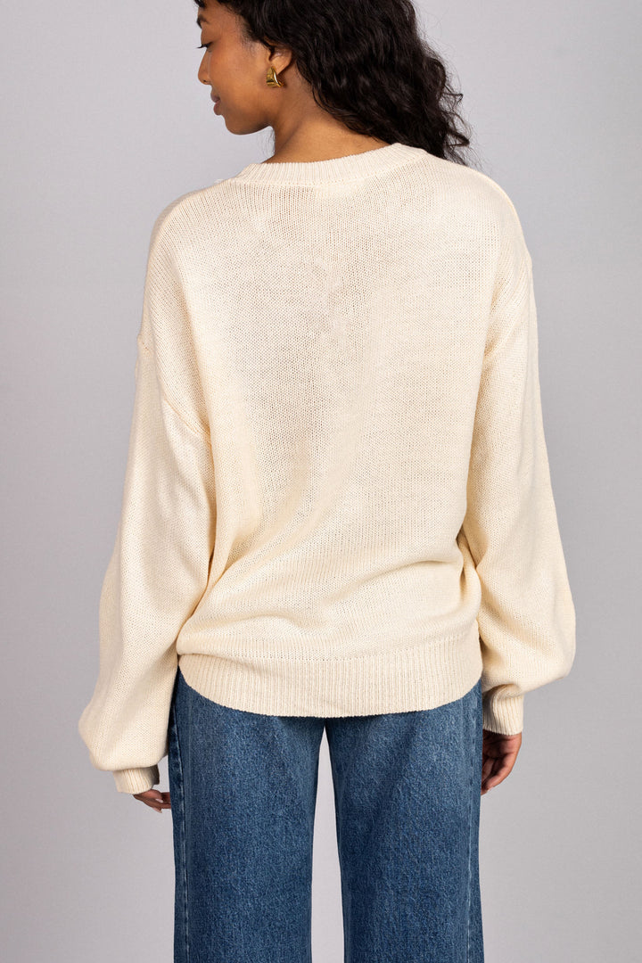 Back view of a soft, cream-colored knit sweater with balloon sleeves and a crew neckline, modeled on a dark-haired person.