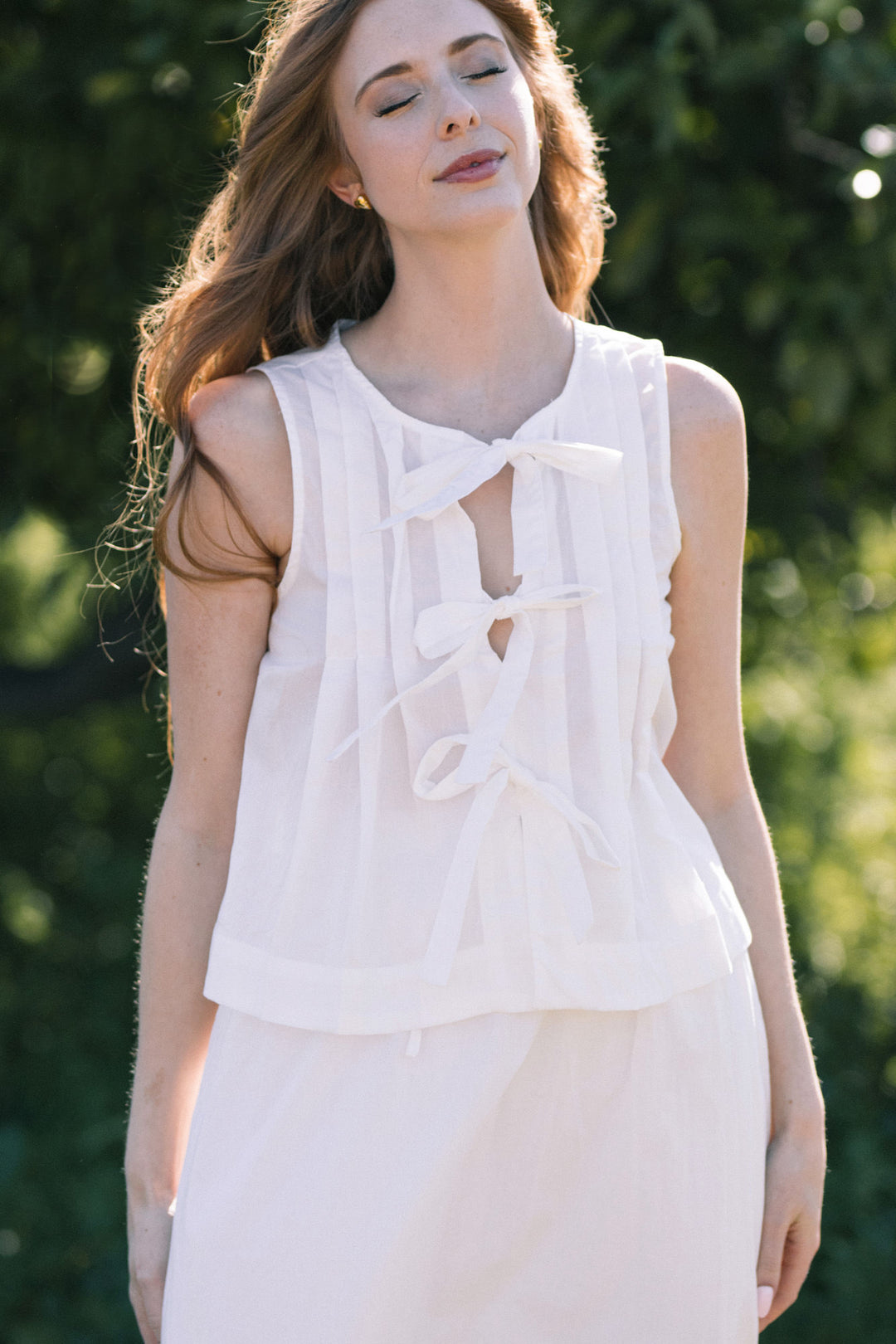 A white sleeveless top with a bow detail at the front neckline, creating a feminine, elegant look.