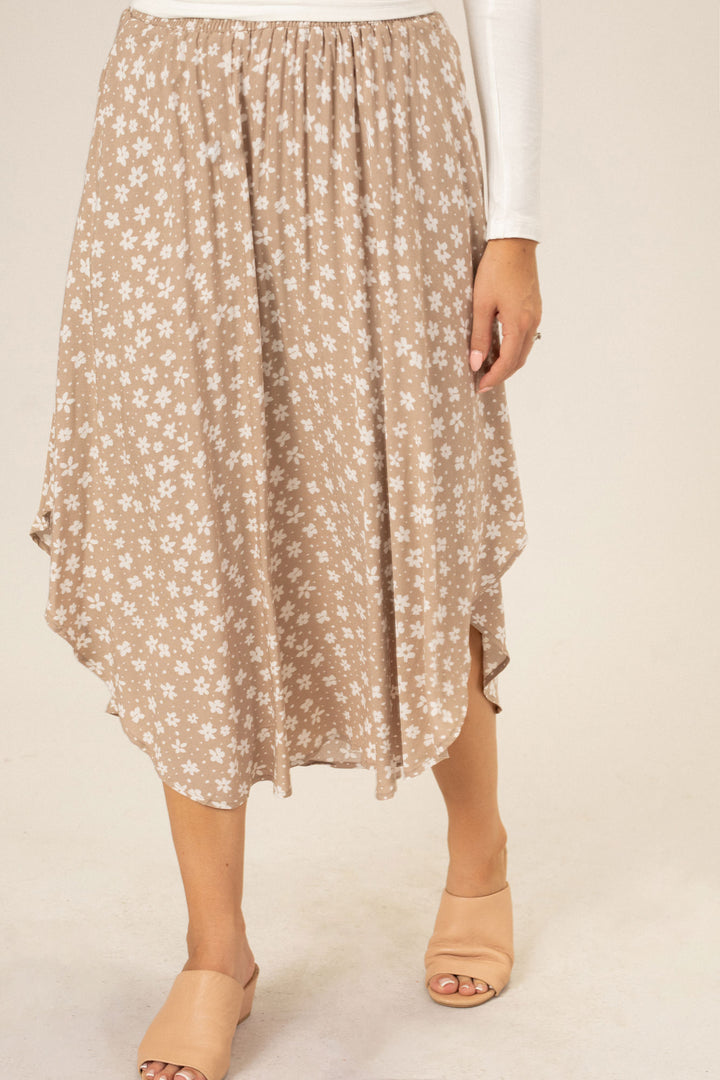 A mid-length, floral print skirt with a rounded hem in a beige and white color scheme, featuring an elastic waistband.