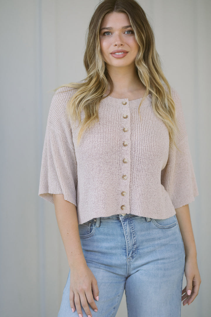 A beige, knitted short-sleeve cardigan with wooden buttons, showcasing a flattering, relaxed fit and a versatile design.