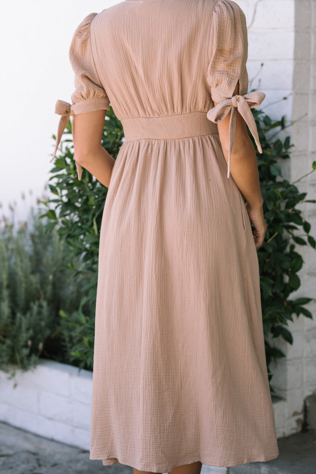 A beige, pleated gauze dress with puff sleeves and tie details at the shoulders, showcasing a relaxed, feminine silhouette.